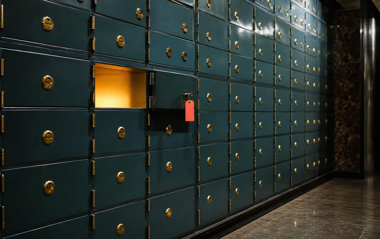 A wall of teal safe deposit boxes with one pulled open, warm light inside, coral tag on the key.