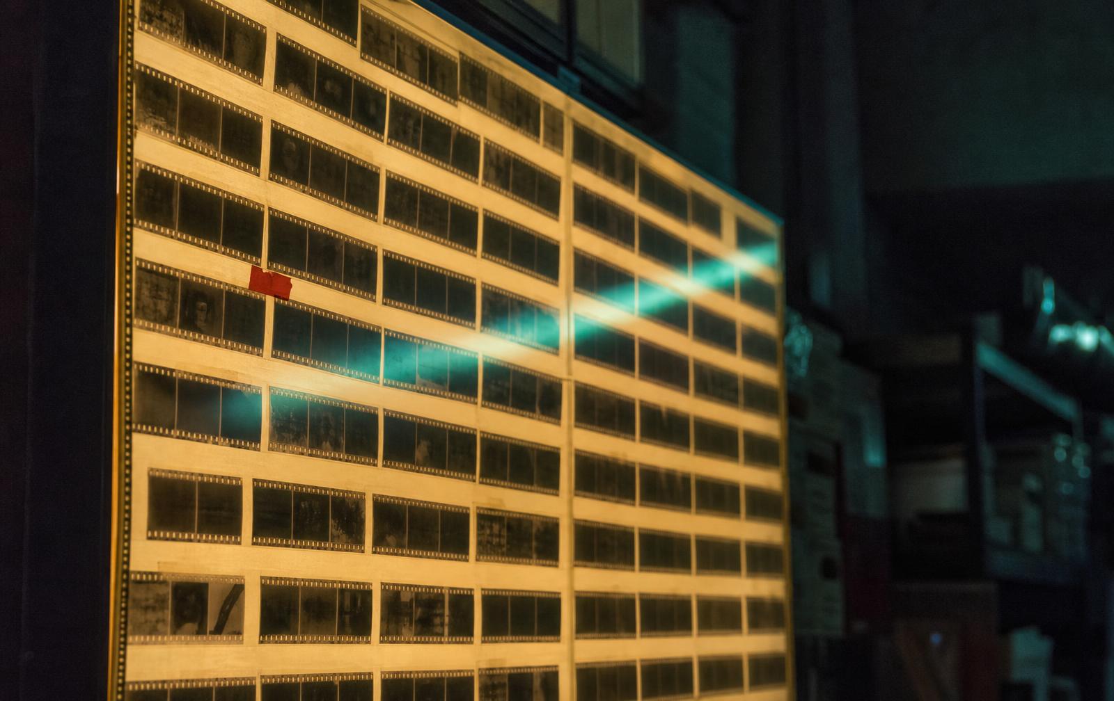 A backlit archive wall of dozens of blank film strips, a cool teal light band sweeping across the grid